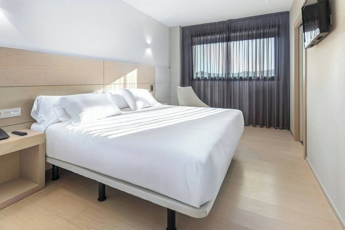 A modern hotel room with a large bed, a bedside table with a phone, and a TV mounted on the wall.