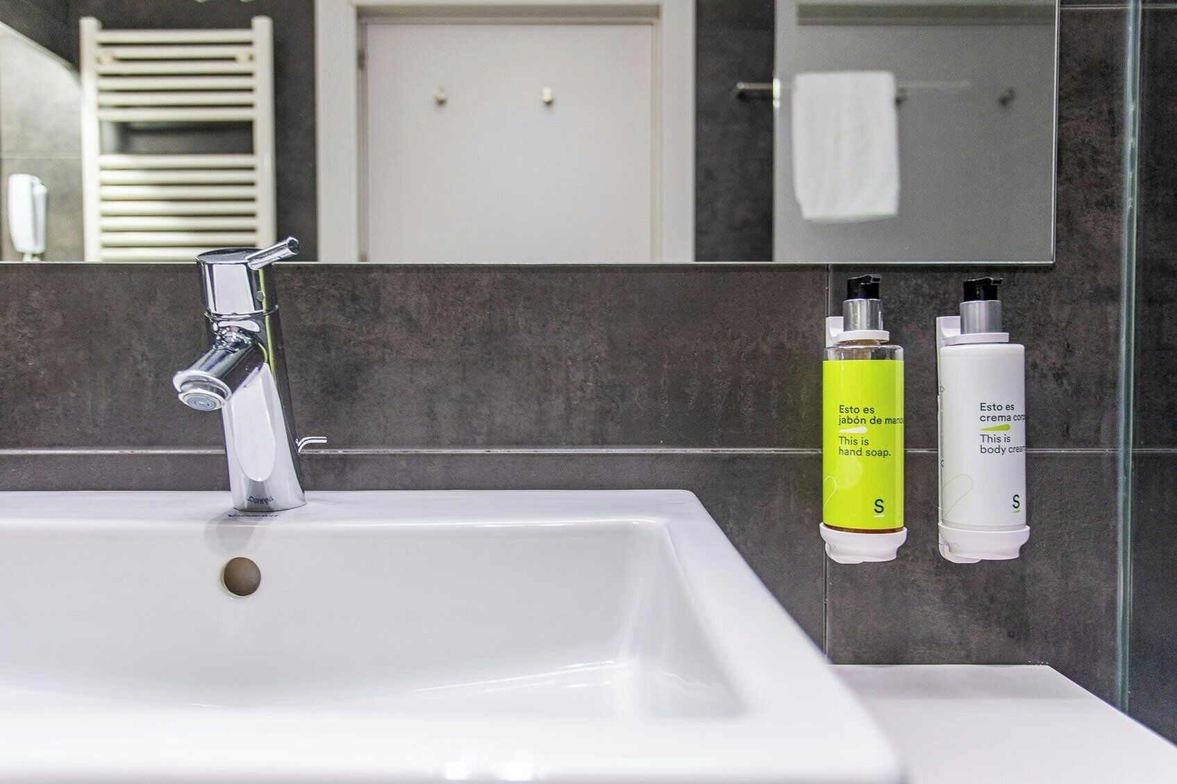 Un baño con un lavamanos blanco, grifo cromado y dos botellas de jabón en la pared.