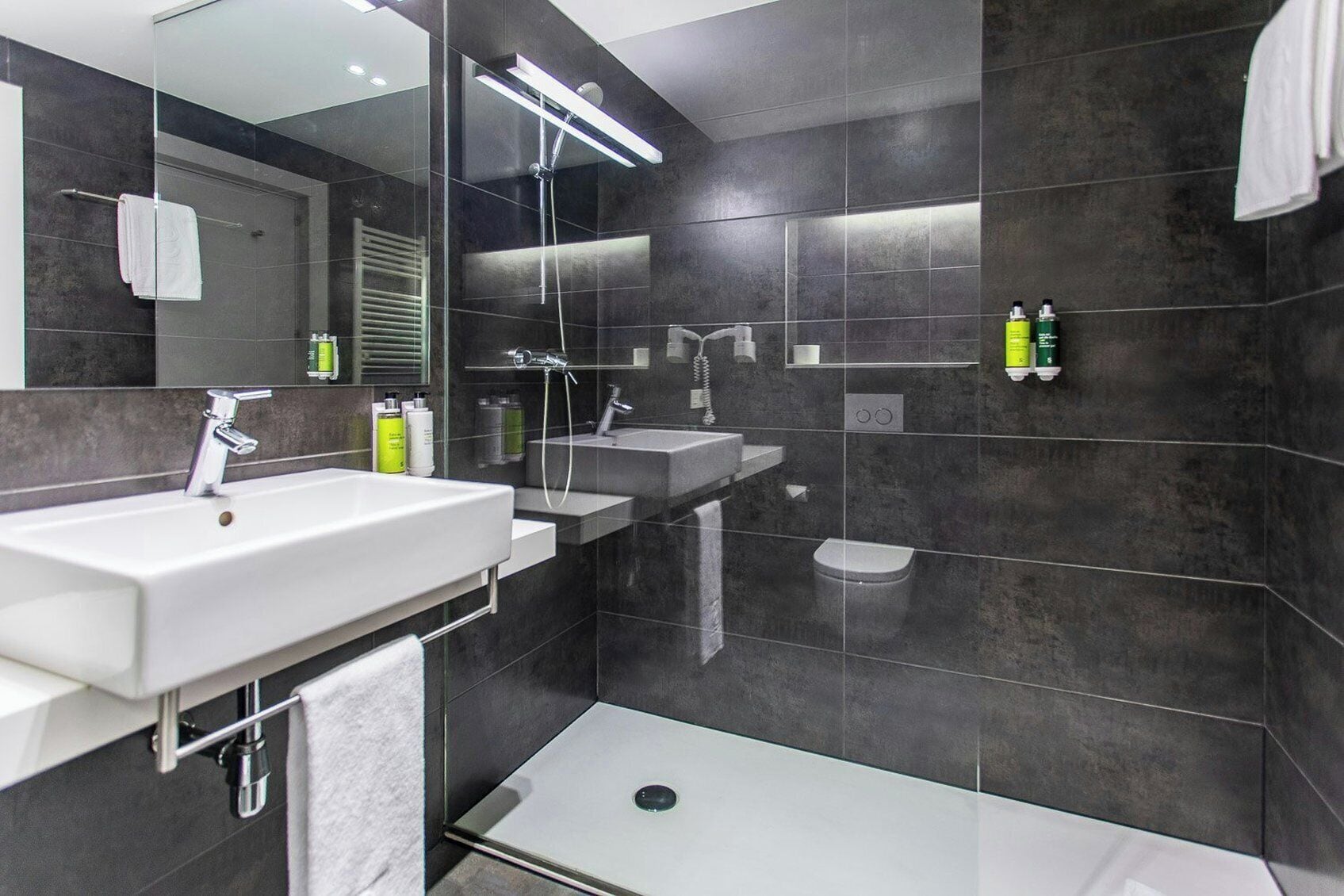 Un baño moderno con un espejo grande, dos lavamanos, ducha y un inodoro.