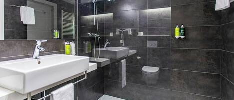 Un baño moderno con un espejo grande, dos lavamanos, ducha y un inodoro.