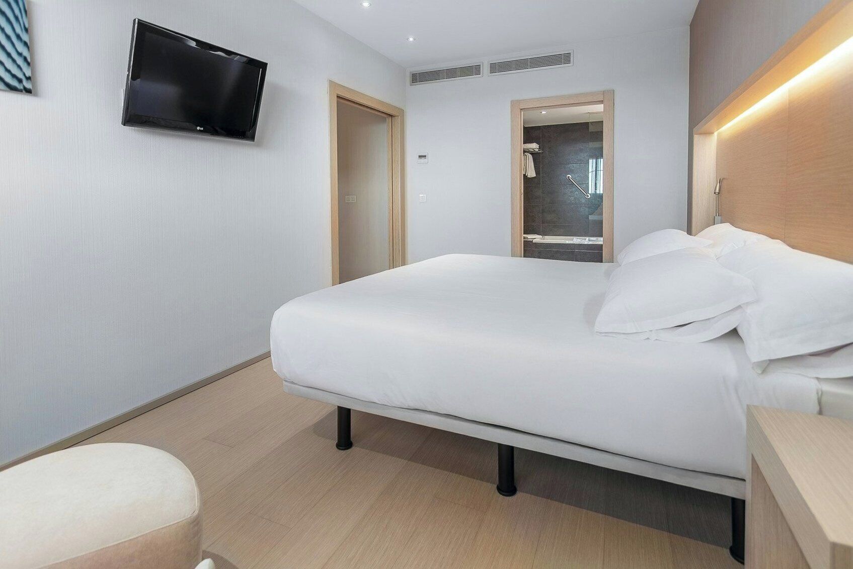 Een moderne hotelkamer met een bed, een televisie, een douche en een houten hoofdeinde.