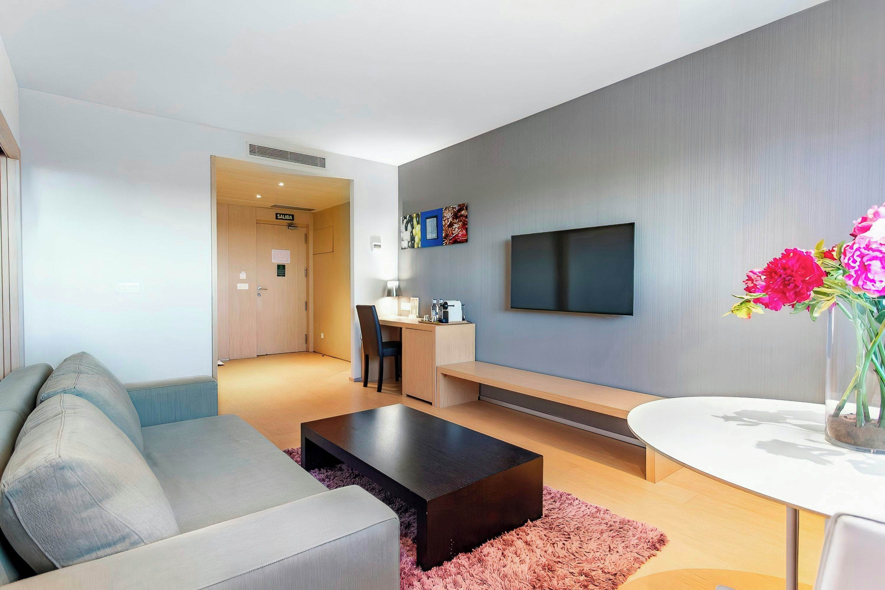 A modern living room with a sofa, a coffee table, a TV, and a small dining area.