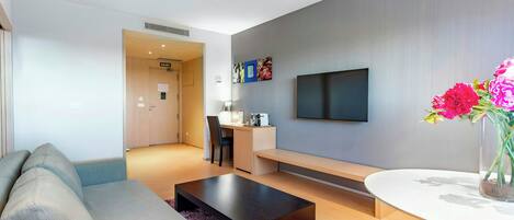 A modern living room with a sofa, a coffee table, a TV, and a small dining area.