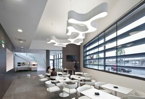 A modern interior with white furniture, a staircase, and large windows offering a view of the street. - Sercotel Hola Tafalla (Tafalla)