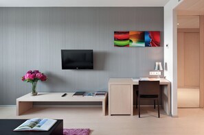 Una camera moderna con TV a schermo piatto montata a parete, una scrivania con sedia, un vaso di fiori e una libreria.