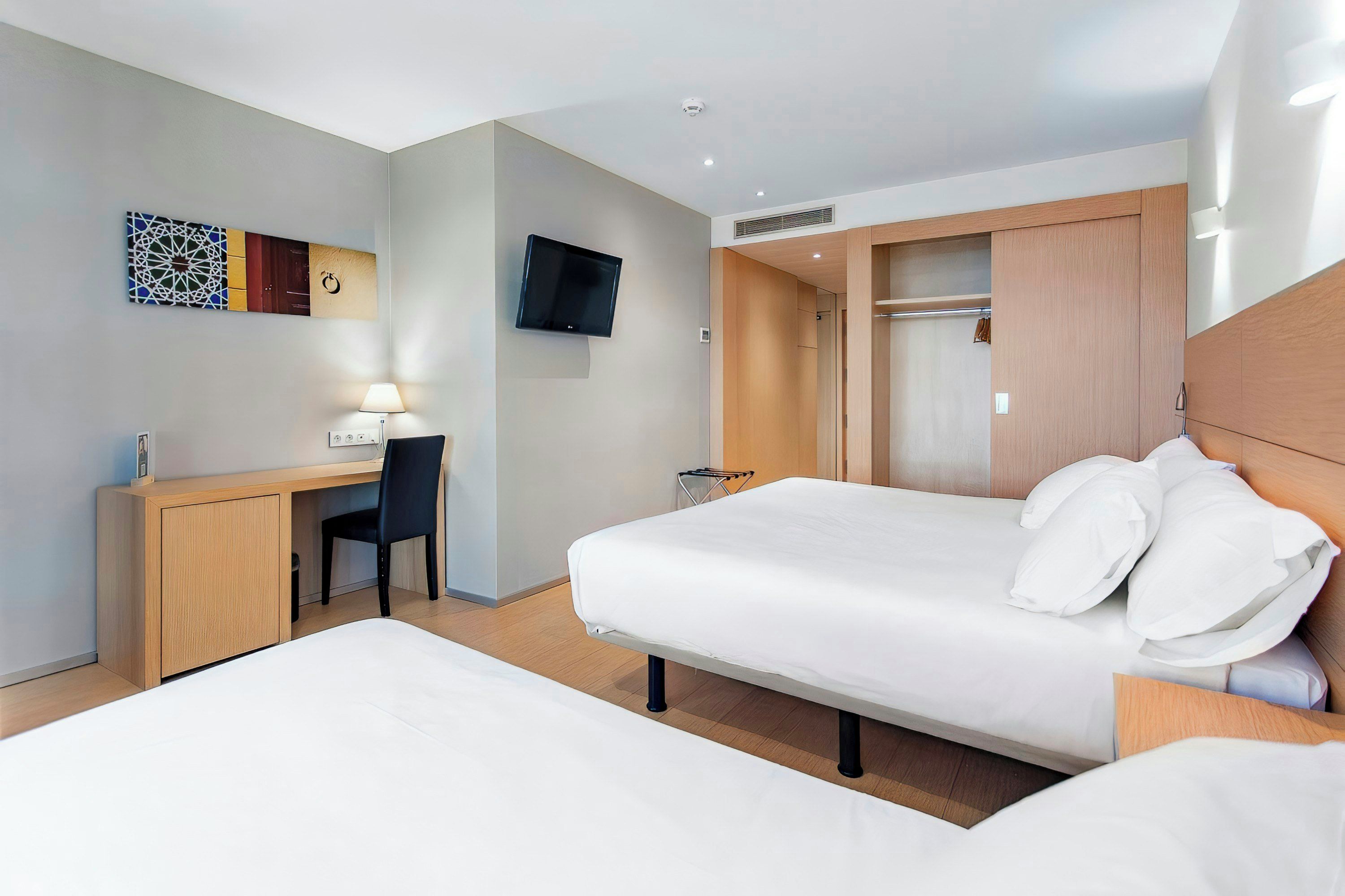 A hotel room with a bed, a desk, a chair, a TV mounted on the wall, and a wardrobe.