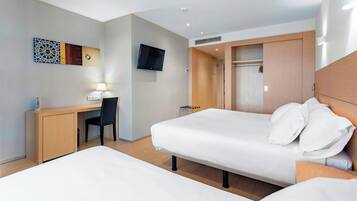 A hotel room with a bed, a desk, a chair, a TV mounted on the wall, and a wardrobe.