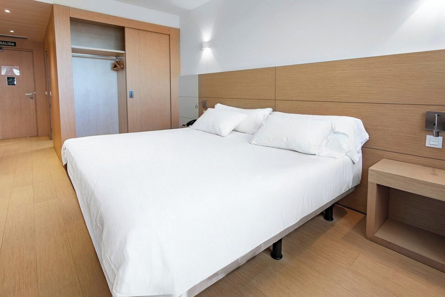 A hotel room with a large bed, wooden headboard, a bedside table, and a wardrobe.