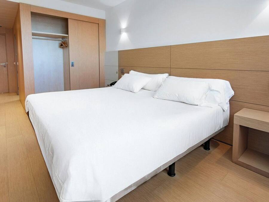 Una habitación de hotel con una cama grande, cabecera de madera, una mesita de noche y un armario.