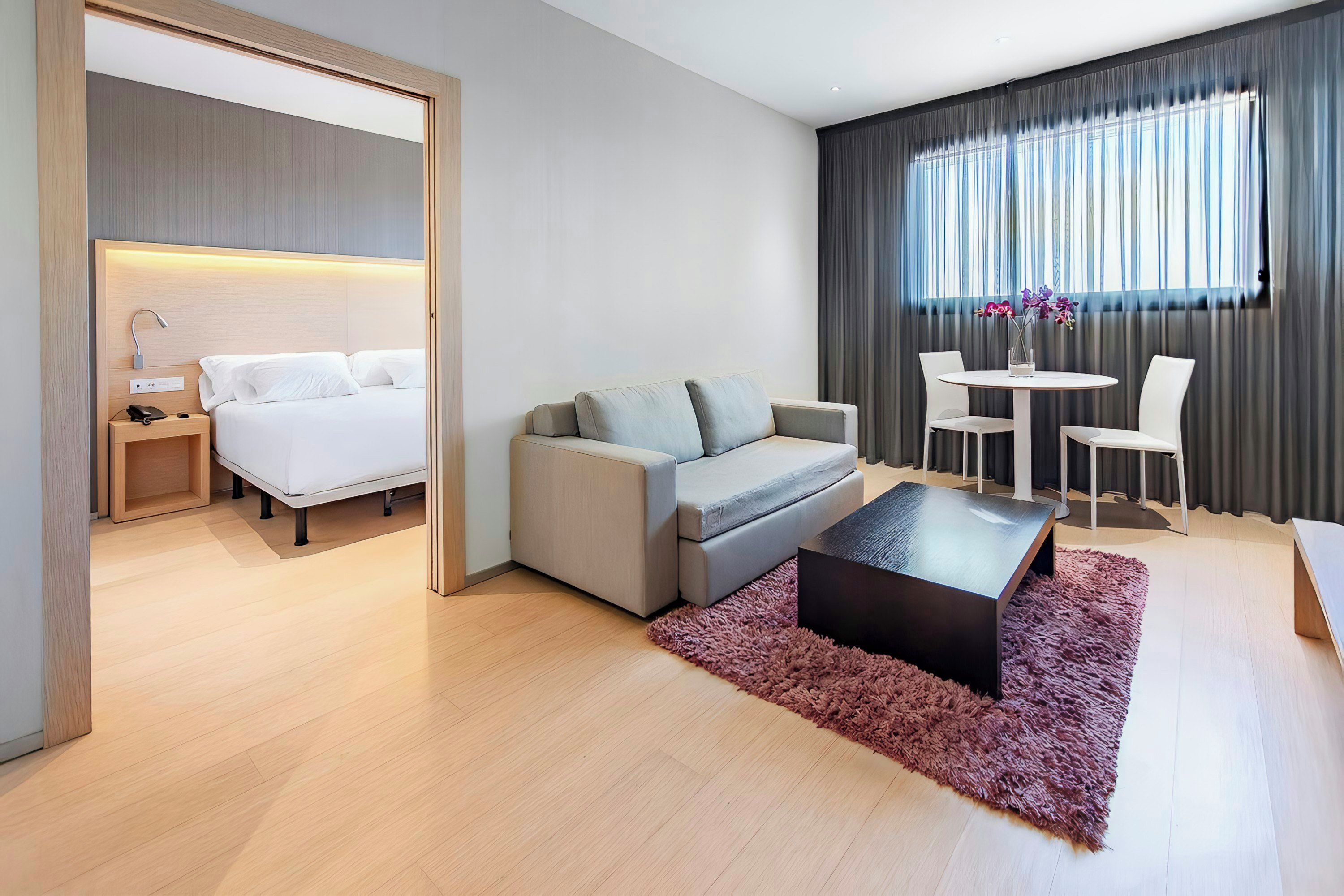 Moderni hotellihuone, jossa on sänky, sohva, sohvapöytä sekä ruokailutila, jossa on tuoleja ja pöytä.