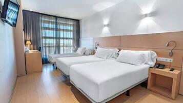 Habitación de hotel con dos camas, televisión, escritorio con teléfono y ventana con cortinas.