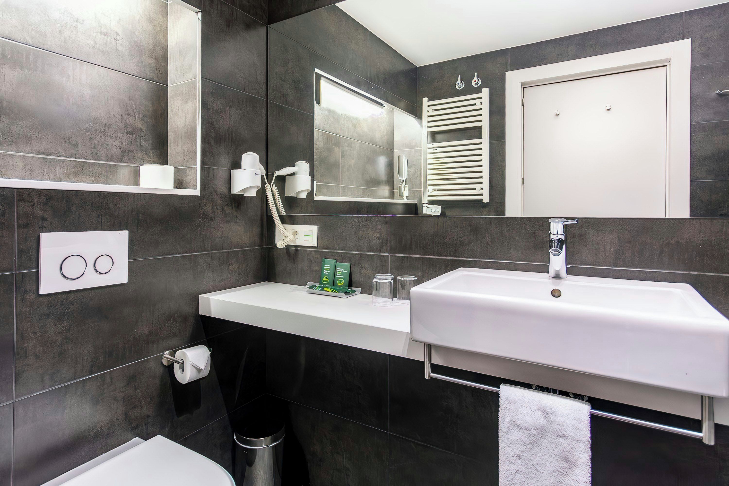 A modern bathroom with a white sink, dark tiled walls, a mirror, and a towel rack.