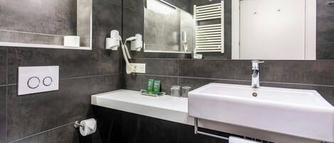 A modern bathroom with a white sink, dark tiled walls, a mirror, and a towel rack.