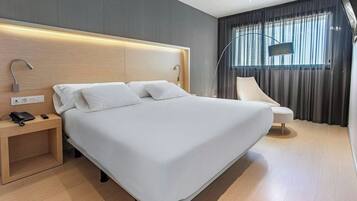 A modern hotel room with a large bed, bedside table with a phone, and a chair.
