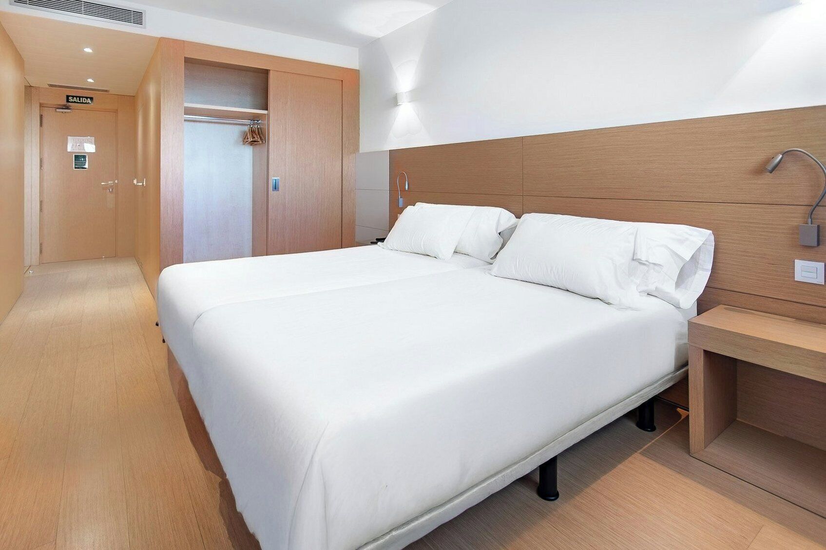 Habitación de hotel con una cama grande, cabecera de madera, mesita de noche y armario.