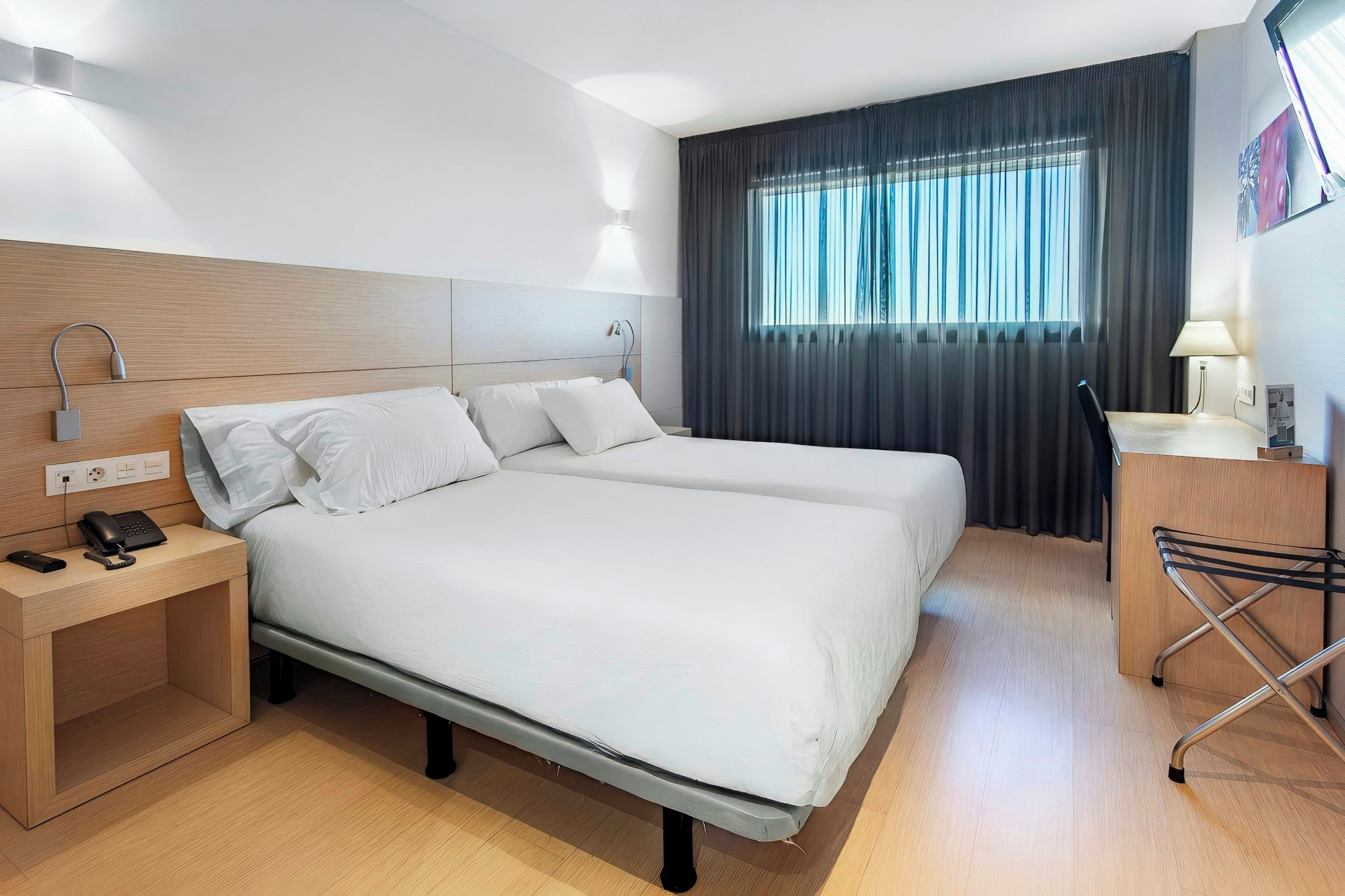 Une chambre d’hôtel avec un lit double, des tables de chevet, un bureau avec une chaise, une lampe et une fenêtre avec des rideaux.