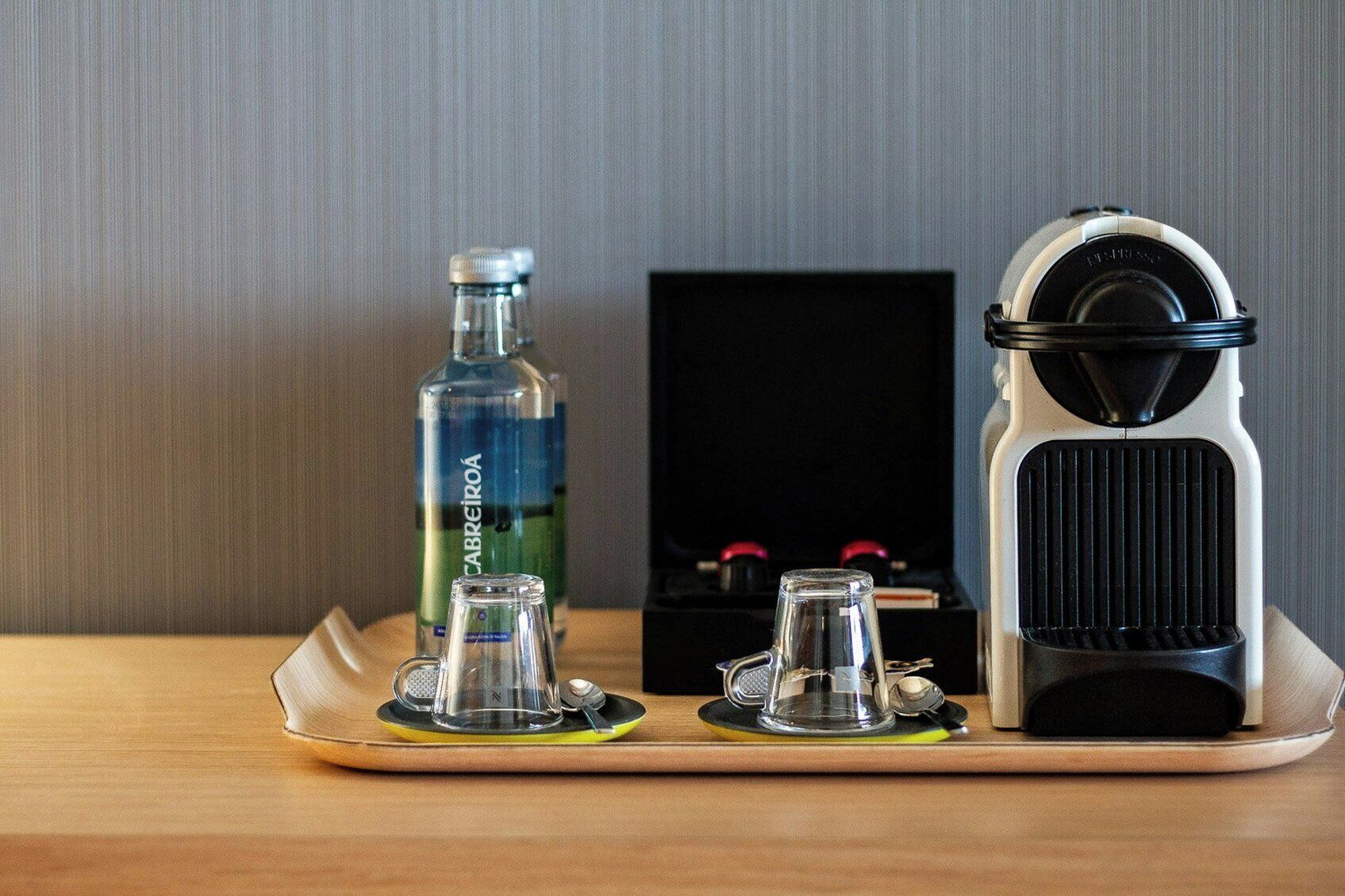 A tray with a glass bottle, a coffee maker, and a coffee grinder on a wooden surface.