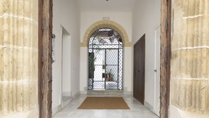 Un couloir doté d’un sol carrelé, d’un chambranle de porte en bois et d’un portail en métal au fond.
