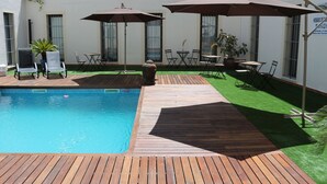 Une piscine avec une plage en bois, des sièges d’extérieur et des parasols.