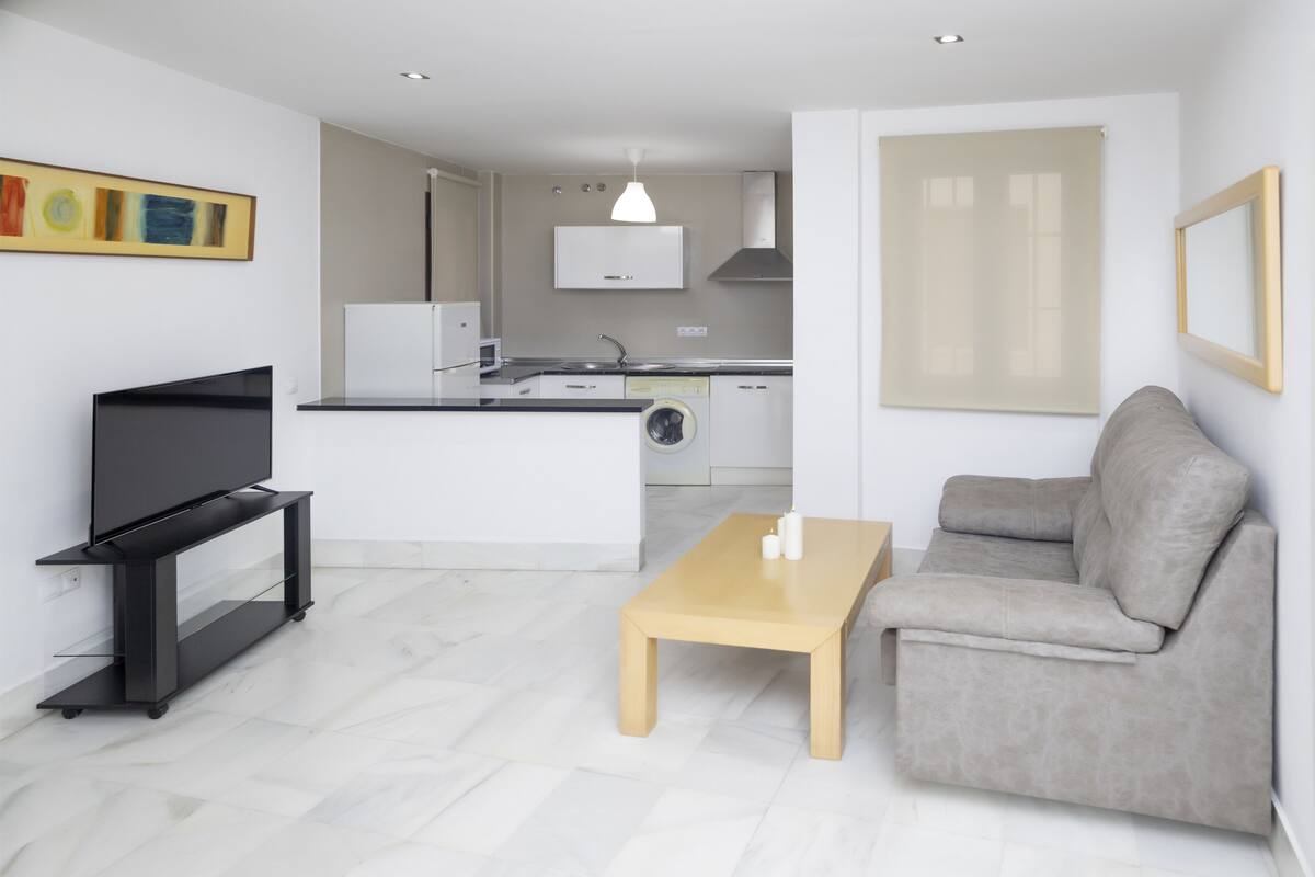A modern living room with a flat-screen TV, a grey sofa, and a wooden coffee table.