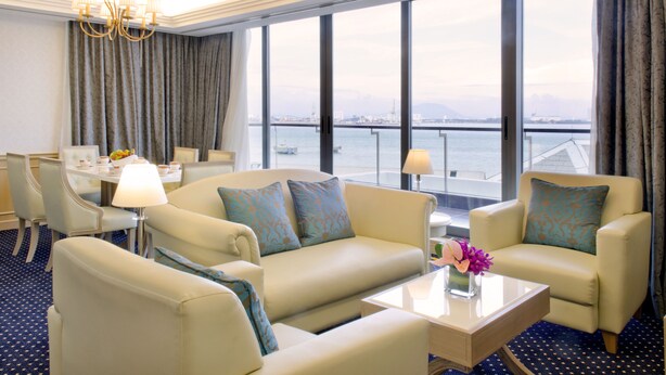 Une chambre d’hôtel dotée d’une grande fenêtre donnant sur la ville, d’un coin repas avec une table et des chaises, et d’un espace détente avec un canapé et des fauteuils.