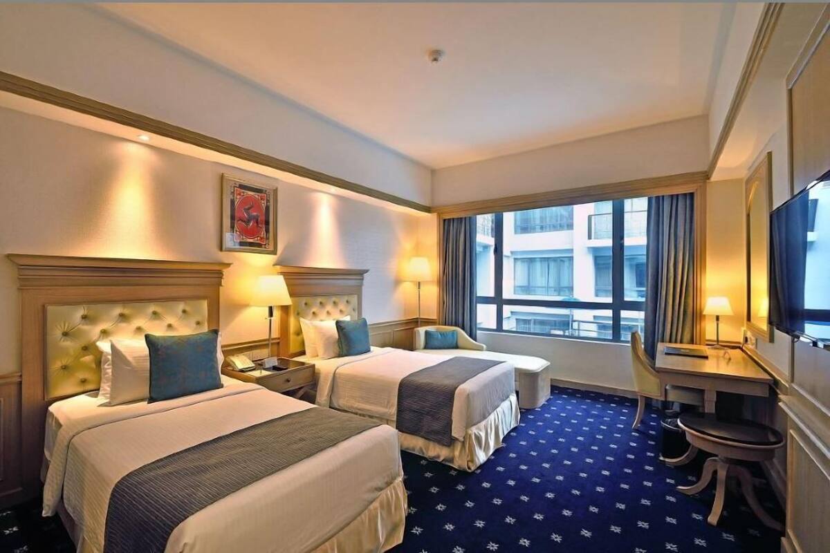 Ein Hotelzimmer mit zwei Betten, einem Schreibtisch, einem Stuhl und einem großen Fenster.