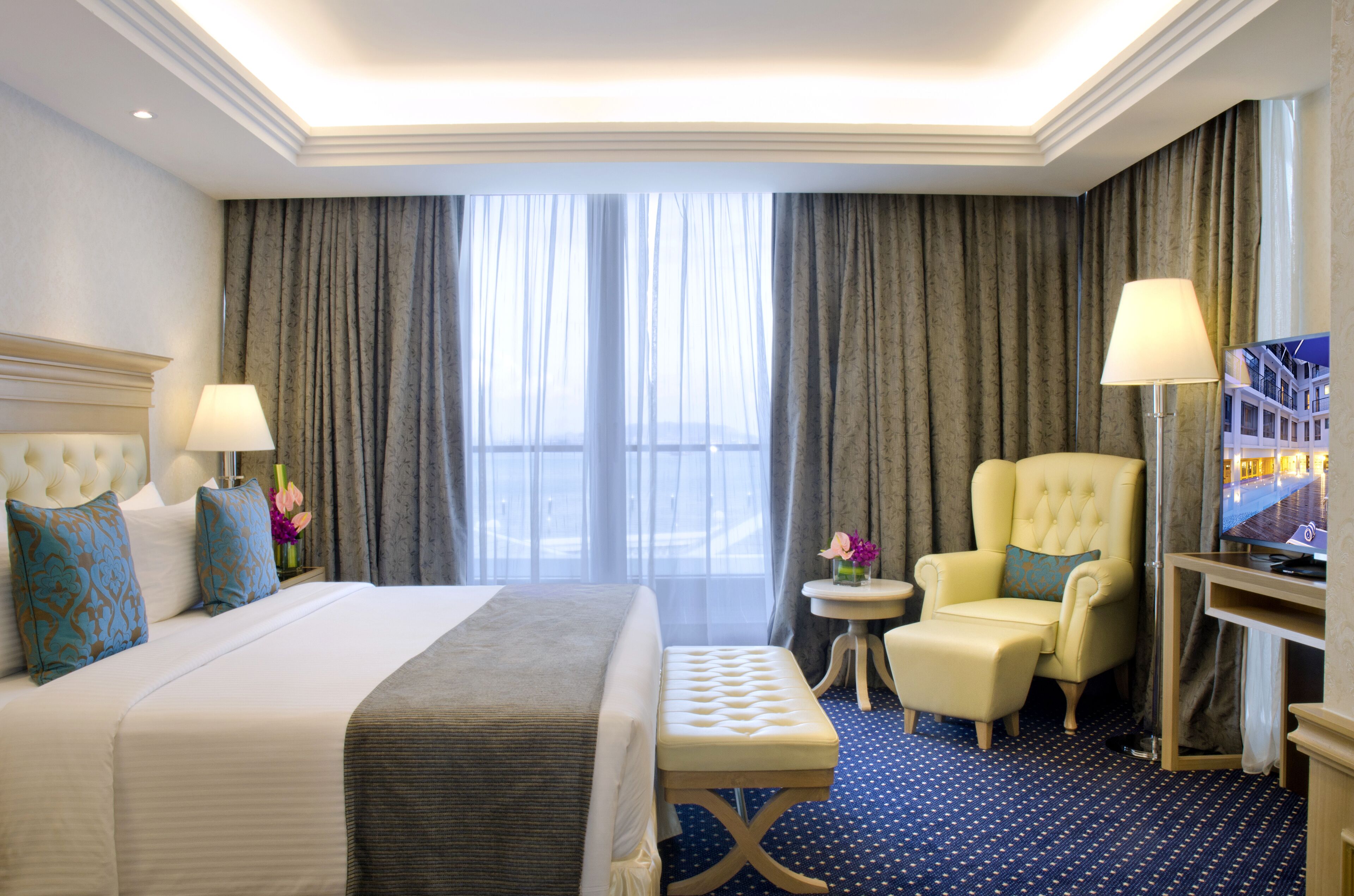 A hotel room with a large bed, two bedside lamps, a chair, a small table, and a TV.