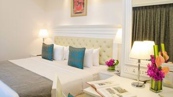 A hotel room with a large bed, two bedside tables, a nightstand, a window with curtains, and a wall-mounted picture.