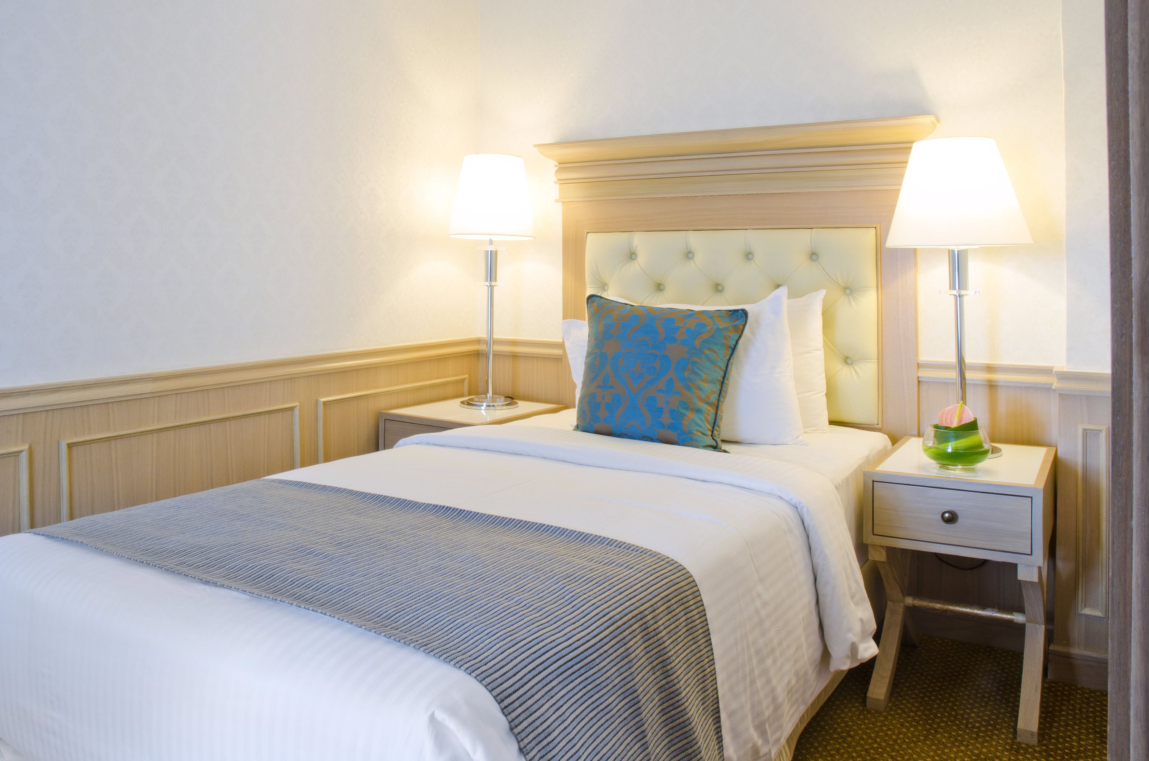 A neatly made bed with a tufted headboard, two bedside lamps, and a small drawer.