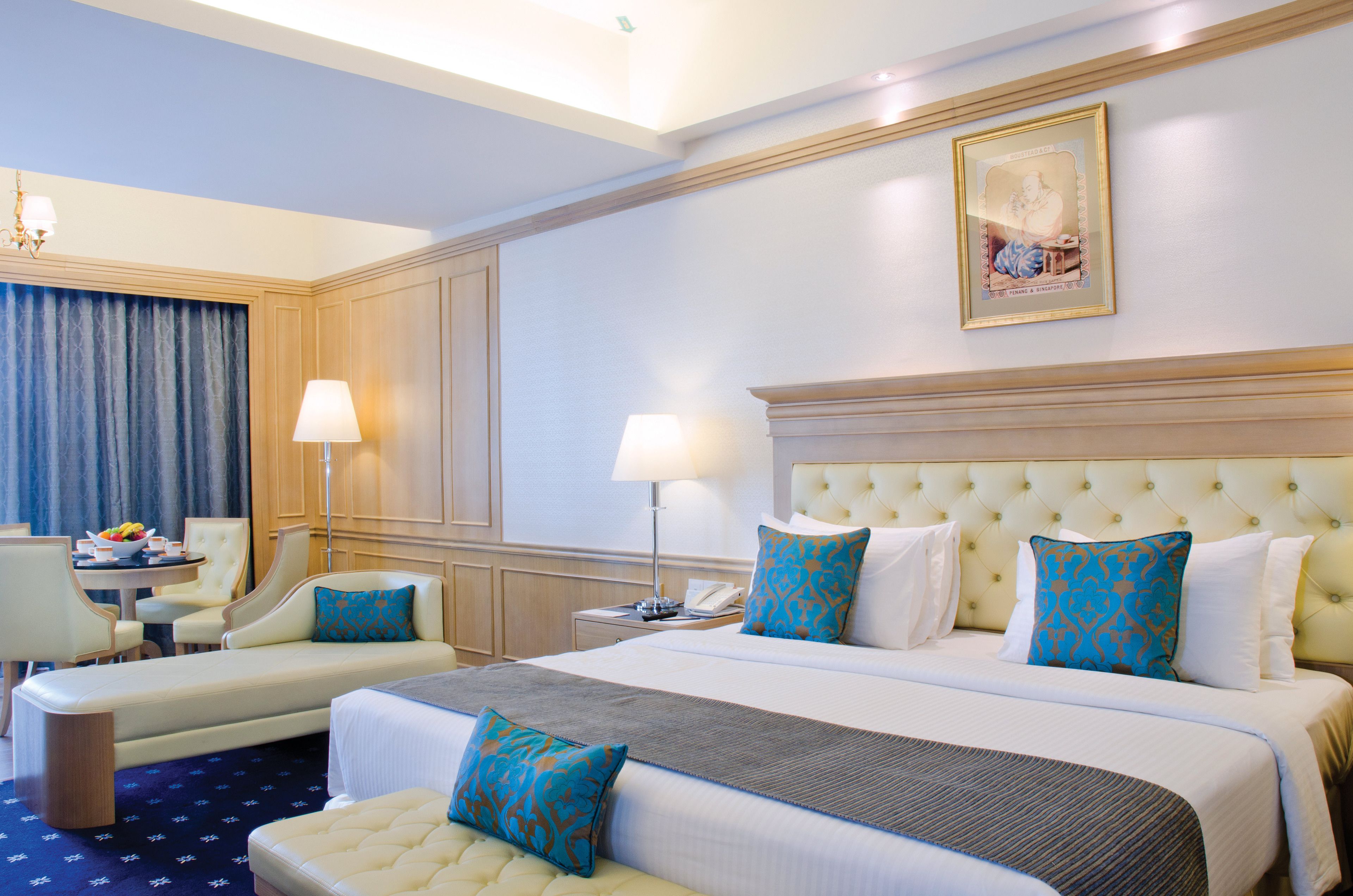 A hotel room with a large bed, two armchairs, a small table, and a desk with a lamp.