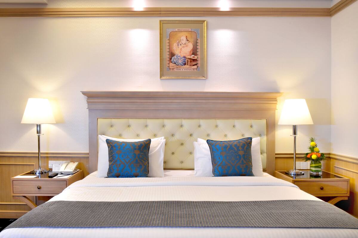 Ein Hotelzimmer mit einem großen Bett, zwei Nachttischen, einem Beistelltisch, einem gerahmten Bild an der Wand und einer Lampe auf jedem Nachttisch.
