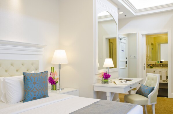 Habitación de hotel con cama, escritorio, silla y baño visible a través de una puerta abierta.