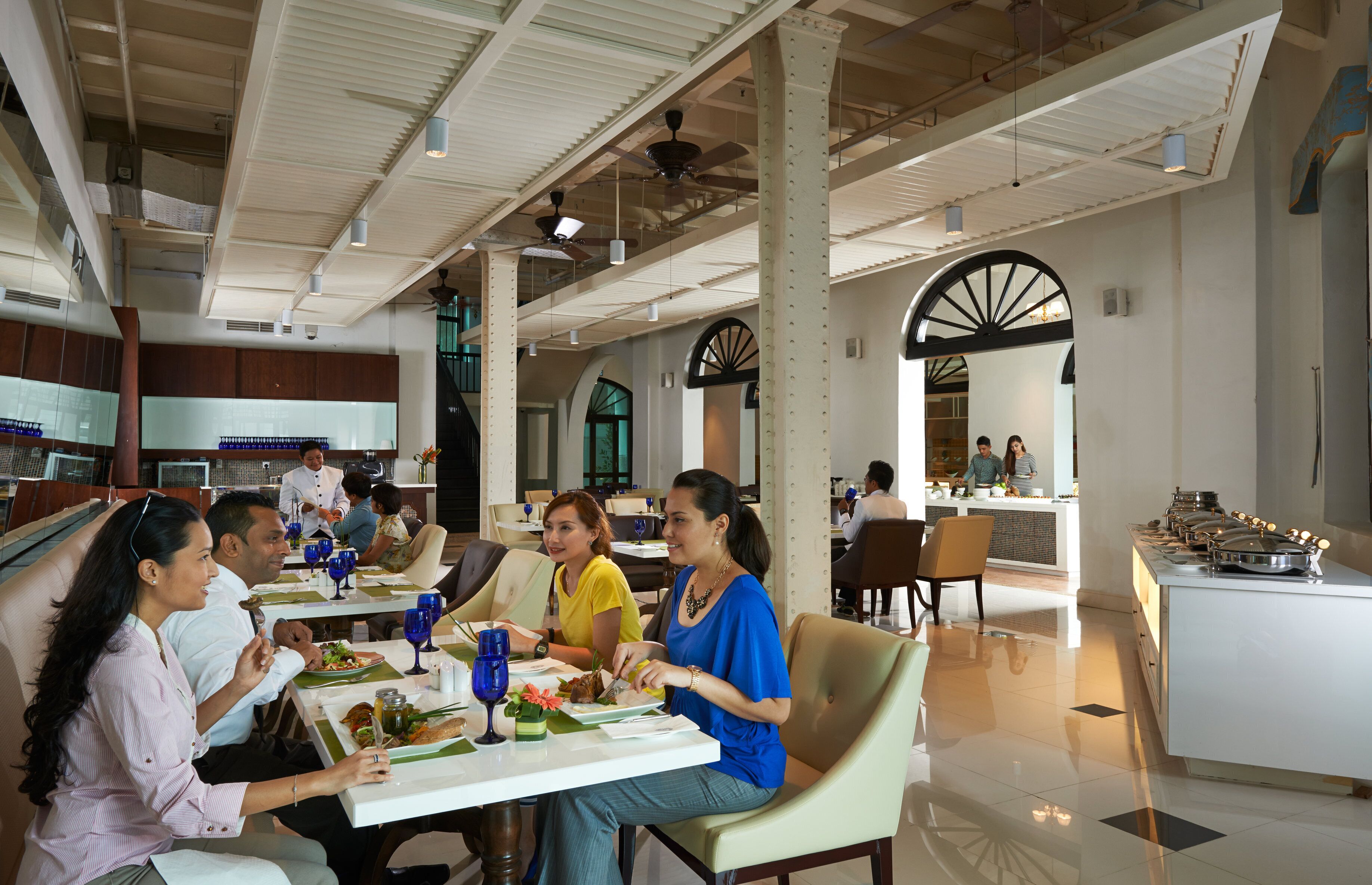 A modern dining area with high ceilings, exposed beams, and a central island with food stations.
