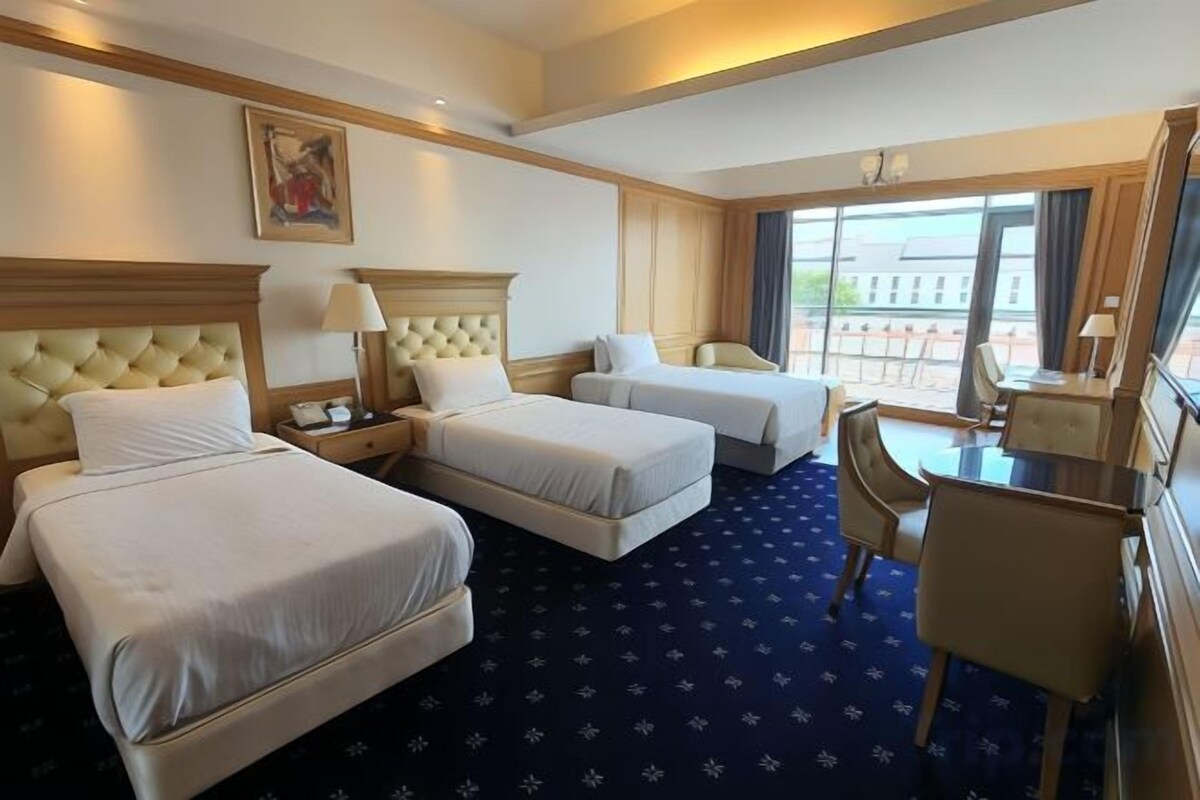 Une chambre d’hôtel avec deux lits, un bureau, une chaise et une grande fenêtre.