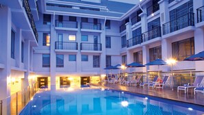Un espace piscine doté de chaises longues et de parasols, entouré de balcons d’hôtel à plusieurs étages.