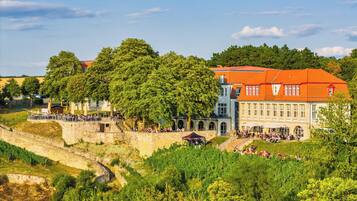 A historic building with a red roof, surrounded by lush greenery and a stone wall.