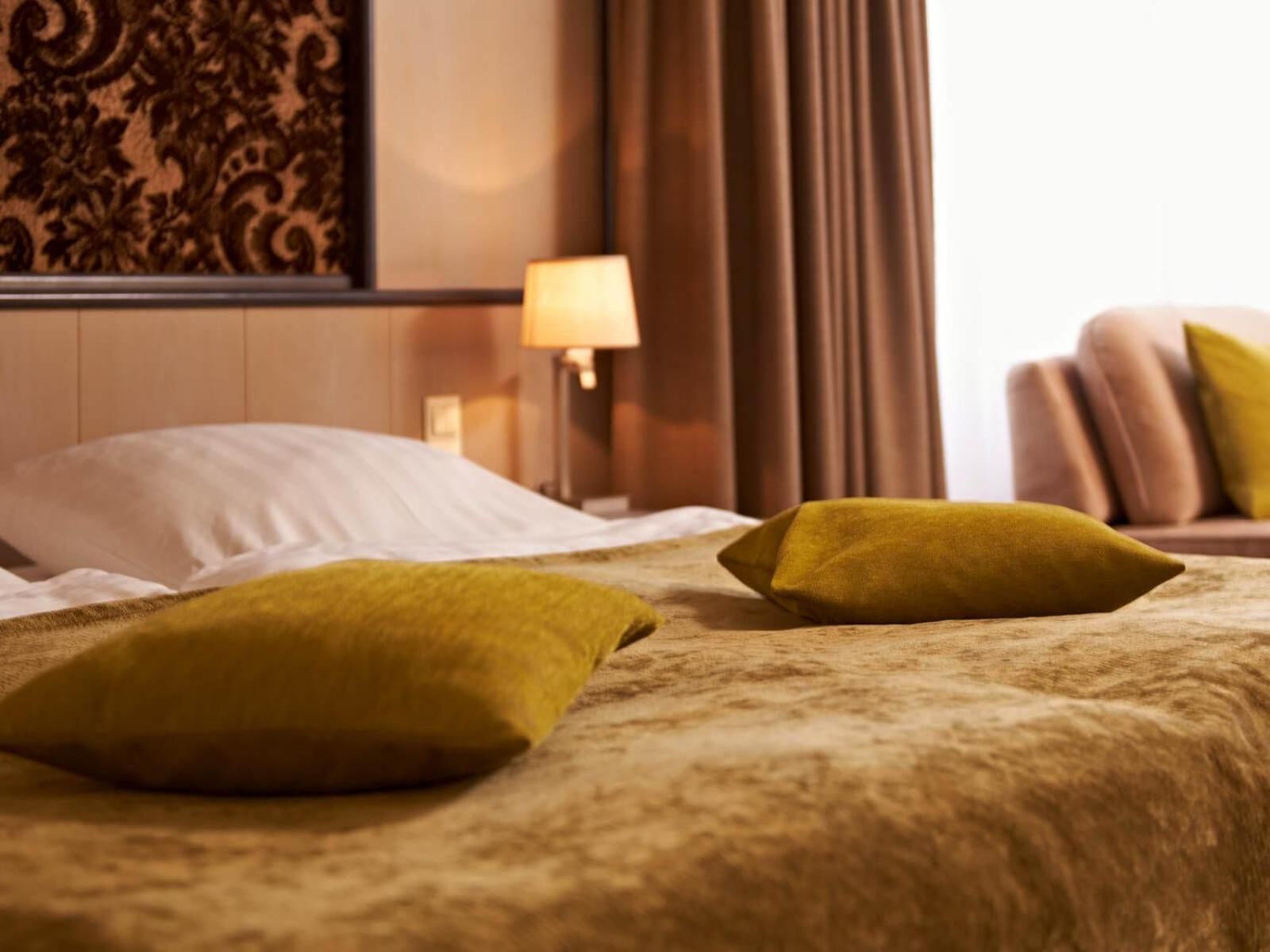 Une chambre d’hôtel avec un lit, deux oreillers, une table de chevet avec une lampe et un rideau.