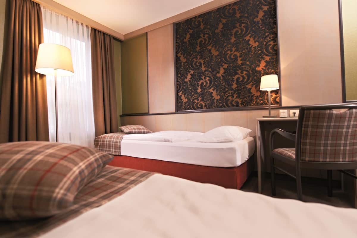 A hotel room with a bed, a desk, a chair, and a lamp.