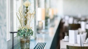 A restaurant with a long counter, a vase with flowers, and a window with a view. - Weinberghotel Edelacker (Freyburg)