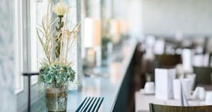 Un restaurant avec un long comptoir, un vase rempli de fleurs et une fenêtre donnant sur un beau paysage.
