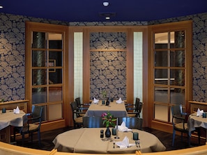 A dining area with a round table, chairs, and a floral wallpaper pattern. - Weinberghotel Edelacker (Freyburg)