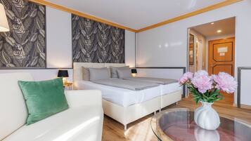 A modern bedroom with a bed, a white sofa, a green pillow, a vase with flowers, and a mirror.