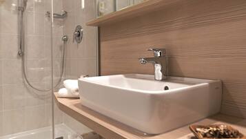Un baño moderno con un lavamanos rectangular grande, un cabezal de ducha de mano y una ducha con mampara de vidrio.