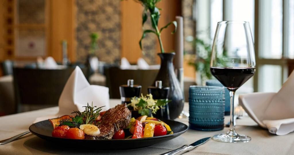 A dining table with a plate of food, a glass of red wine, and a vase with flowers.