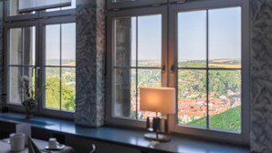 A room with a large window offering a view of a town. - Weinberghotel Edelacker (Freyburg)