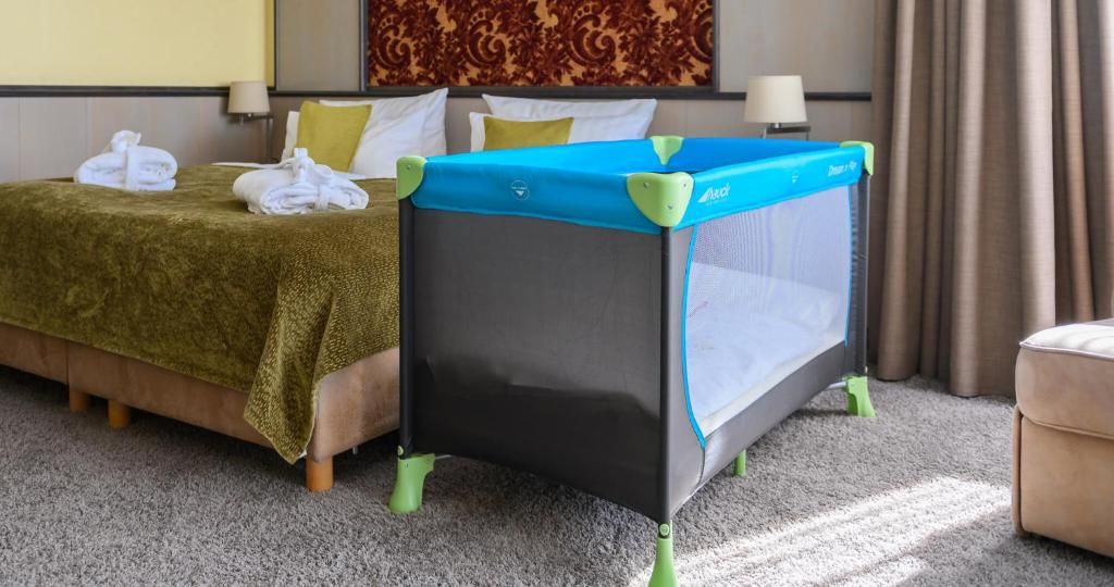 A hotel room with a bed, a crib, and a small table with a lamp.