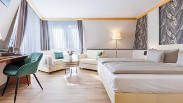 Habitació d'hotel amb un llit, un escriptori, una cadira, un sofà i una taula petita amb un ram de flors.