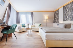 A hotel room with a bed, a desk, a chair, a sofa, and a small table with a vase of flowers. - Weinberghotel Edelacker (Freyburg)
