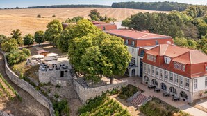 Een historisch gebouw met een rode dakbedekking, omringd door een stenen muur en weelderige begroeiing.