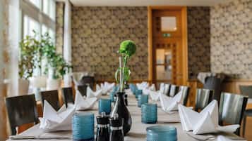 A dining table set with blue glassware, white napkins, and a black vase with a green plant.